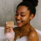 Woman in a bathtub holding a bar of soap with a neutral background