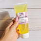 Hand holding a tube of Irawo Beauty Complex Cleanser Gel on a wooden surface